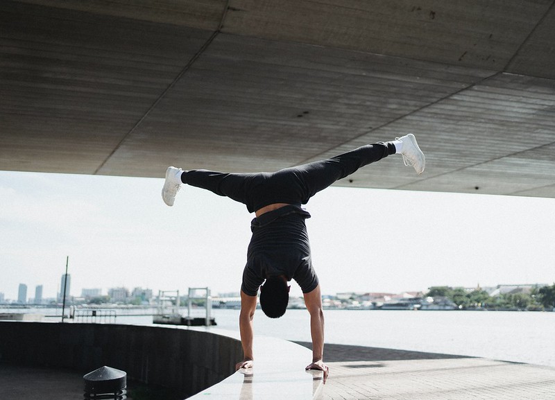 Een man doet een handstand op een rand van een betonnen constructie met uitzicht op het water